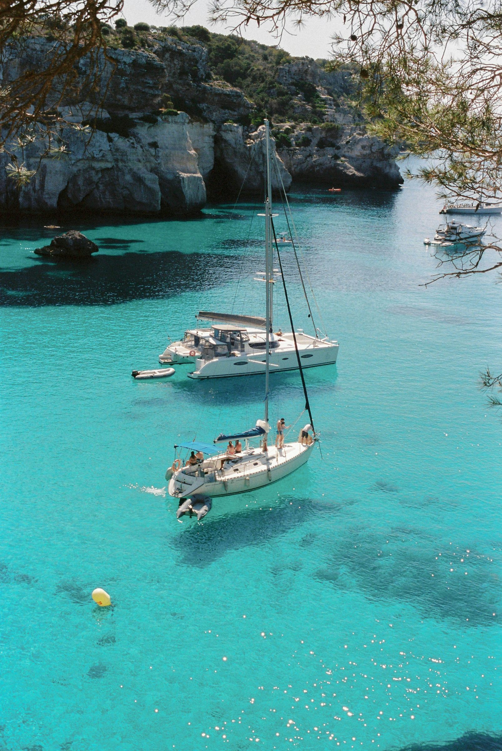 Sailboats anchored in a calm turquoise Mediterranean cove